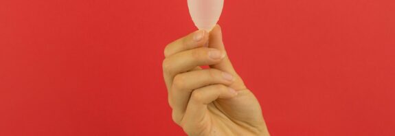 Hand holding menstrual cup with a red background