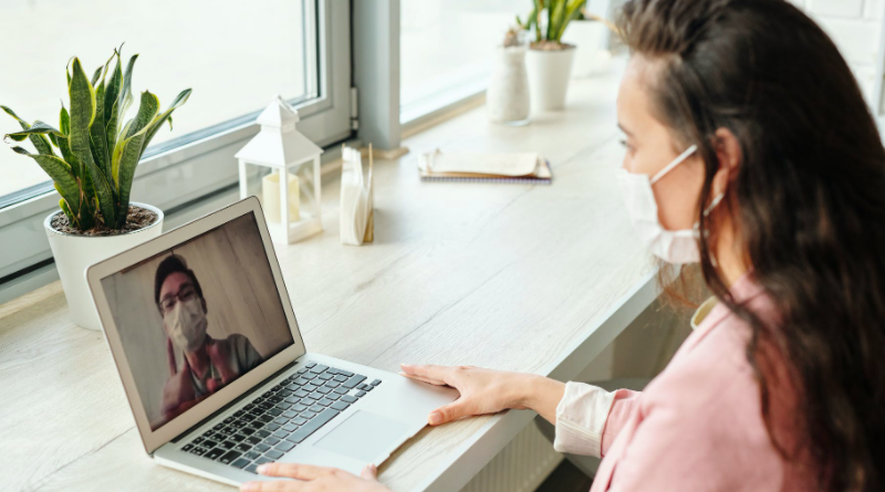 Young woman wearing facemask talking via a laptop video call with a health care professional, also in a facemask