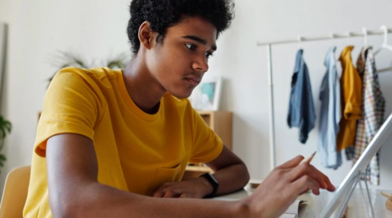 Young man using a tablet at a desk in a bedroom, looking a bit anxious