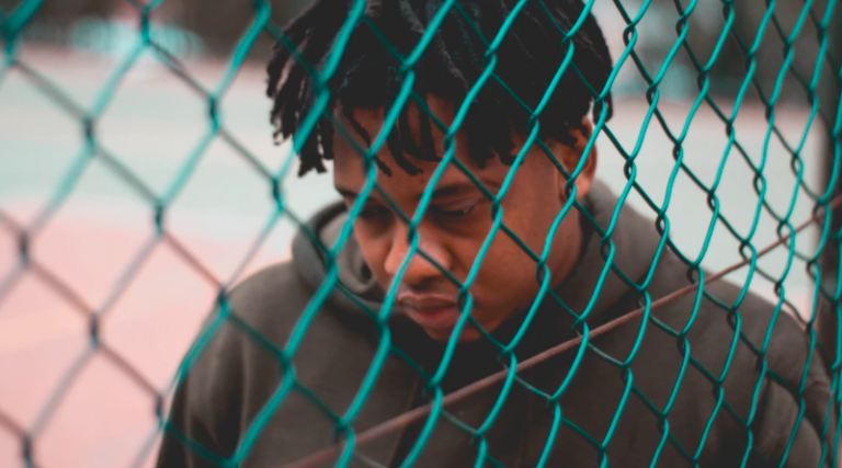 Young person looking sad standing behind the net of a sports court