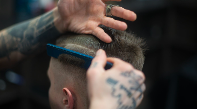 A haircut taking place in a barbers, head of the client and hands of the barber using a comb on the client's hair