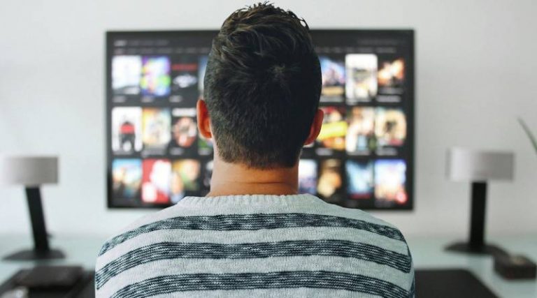 Person in stripy jumper with their back to the camera watching TV